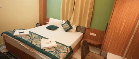 A neatly made bed with a patterned bedspread, a bedside table with a remote control, and a chair in a room with green walls and wooden accents.