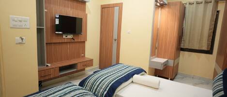A hotel room with two beds, a TV mounted on a wooden cabinet, a bathroom with a shower curtain, and a small desk with a mirror.