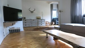 Una sala de estar moderna con piso de madera, un televisor de pantalla plana en la pared, un sofá, una mesa de centro y un adorno decorativo con cuernos de ciervo.