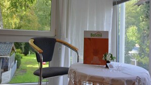 A room with a view of a green landscape, a chair, a table with a lace tablecloth, and a sign with the name 'Belvilla'. - Schönow Forest Apartment (Berlin-Schönow)
