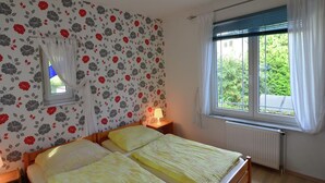 A bedroom with two beds, floral wallpaper, a window with curtains, and a radiator. - Schönow Forest Apartment (Berlin-Schönow)