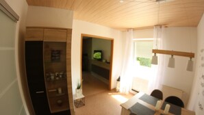 A room with a wooden ceiling, a dining table with chairs, a small kitchen area, and a television in the background. - Wohnung am Diemelsee bei WillingenWinterberg (Diemelsee)
