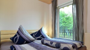 A bedroom with a wooden headboard, a large window with curtains, and a bed with patterned bedding. - Wohnung am Diemelsee bei WillingenWinterberg (Diemelsee)