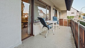 A balcony with a table and chairs, a sliding glass door, and a view of the street and buildings. - Exclusives Ferienhaus in Frankenau im Sauerland (Frankenau)