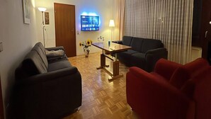 A living room with a sofa, a red armchair, a wooden coffee table, and a TV mounted on the wall. - Exclusives Ferienhaus in Frankenau im Sauerland (Frankenau)
