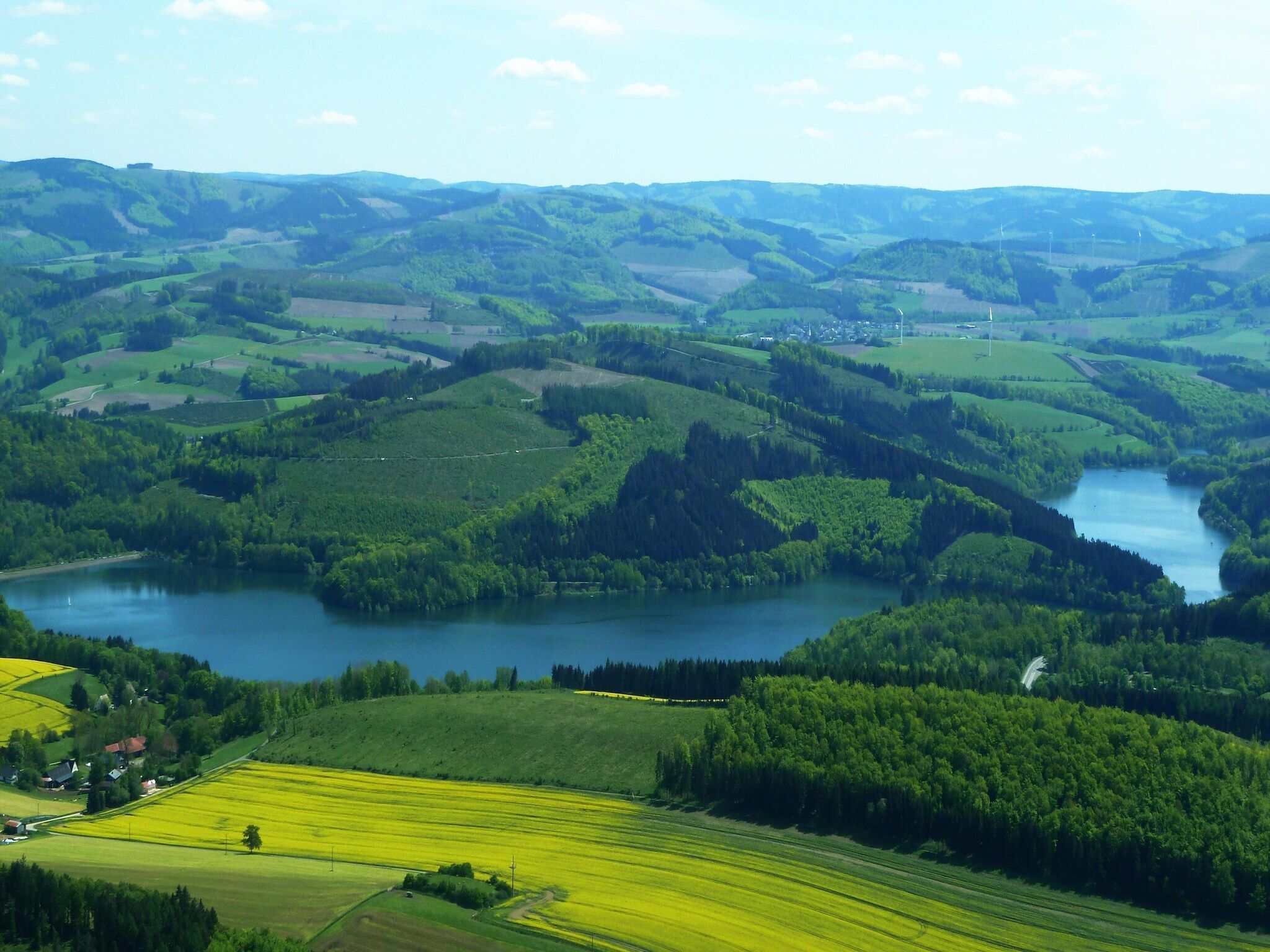 A panoramic view of a valley with a river, fields, and scattered buildings.