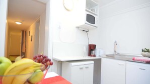 Una cocina con armarios blancos, microondas, cafetera y pileta. Hay un cuenco con fruta en la encimera.