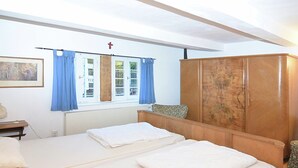 Une chambre avec deux lits, une armoire en bois, une fenêtre avec des rideaux bleus et un tableau accroché au mur.