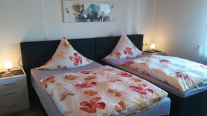 Een tweepersoonsbed met bloemenbedrukking en passende kussens, een nachtkastje met lamp, en een kunstwerk aan de muur boven het bed.