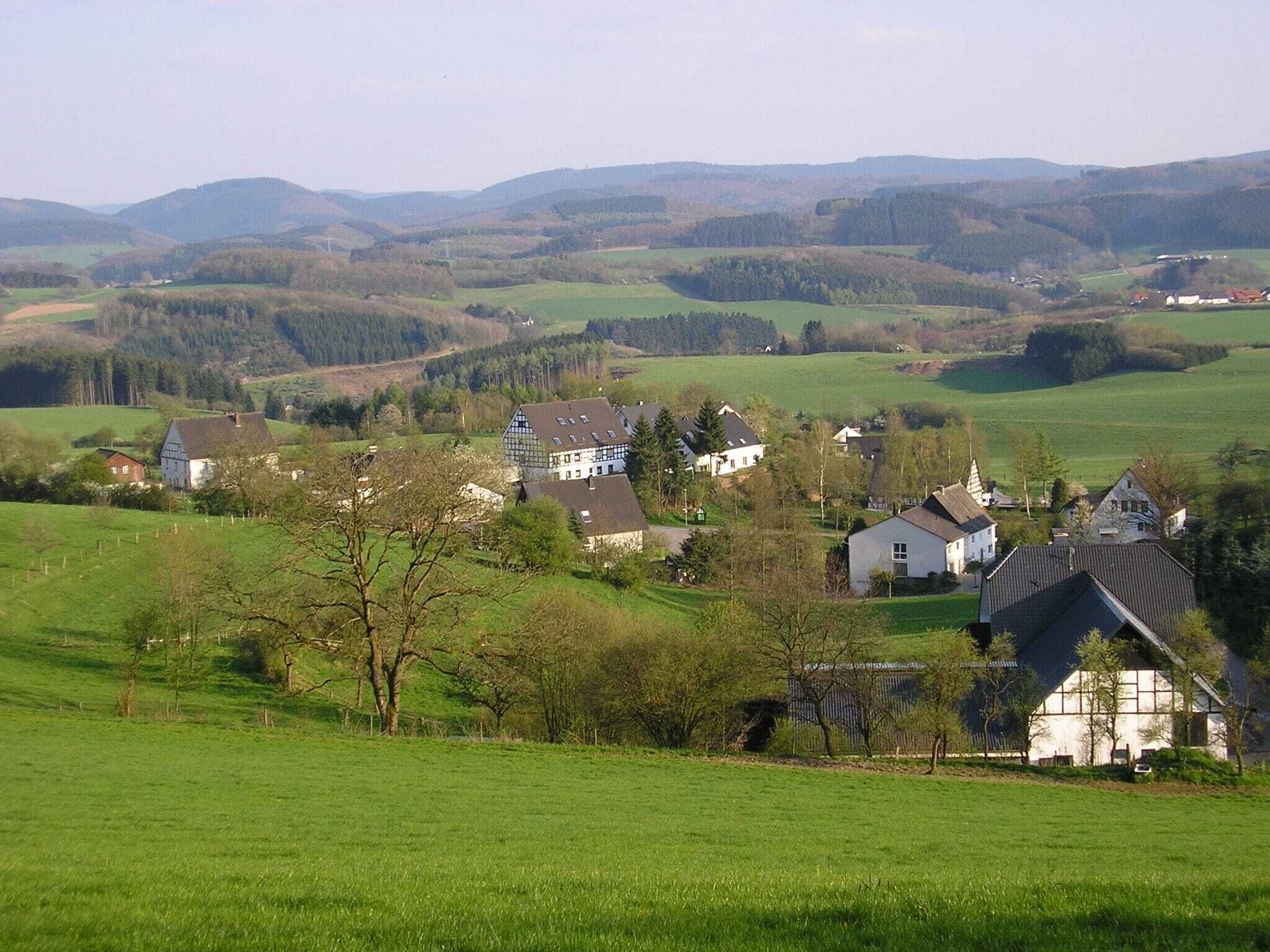 A rural village with houses on a hillside, surrounded by green fields and hills.
