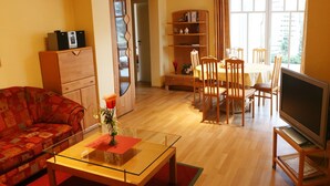 A living room with a sofa, a glass coffee table, a dining table with chairs, a TV on a stand, and a bookshelf. - Stilvolle Wohnung in Madfeld mit eigener Terrasse (Brilon-Madfeld)