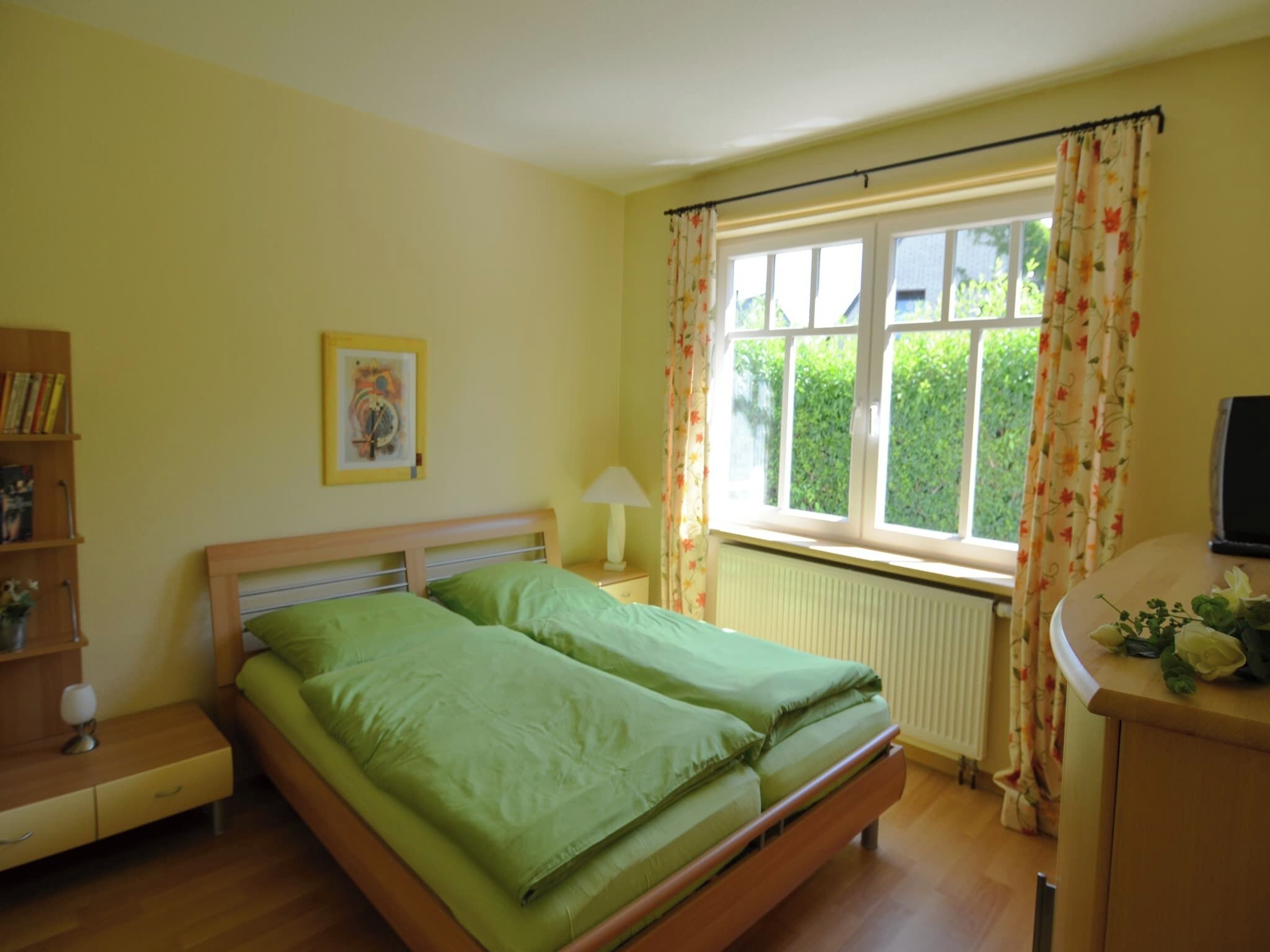 Un dormitorio con una cama, una mesita de noche, una lámpara, una ventana con cortinas y un radiador.