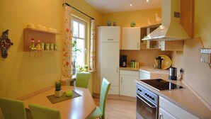 A compact kitchen with a dining table, chairs, a stove, and a window with curtains. - Stilvolle Wohnung in Madfeld mit eigener Terrasse (Brilon-Madfeld)