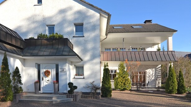 A two-story house with a white exterior, a front porch, and a brick driveway. - Stilvolle Wohnung in Madfeld mit eigener Terrasse (Brilon-Madfeld)