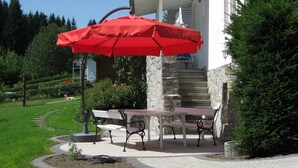 Eine Terrasse mit einem roten Sonnenschirm, zwei Bänken und einer Steintreppe, die zu einem Gebäude führt.