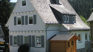 Ein zweistöckiges Haus mit Satteldach, einer Holztgarage und einem kleinen Gartenhaus.