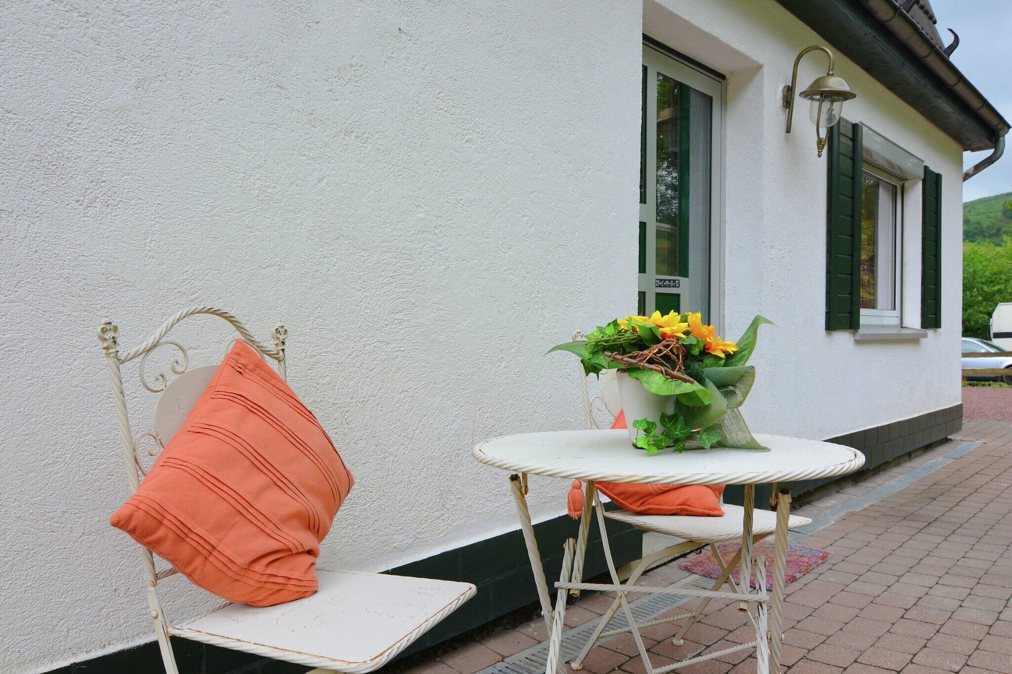 Een wit gebouw met een klein terras, inclusief een witte tafel en twee stoelen met oranje kussens.