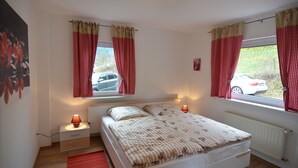 A bedroom with a bed, two bedside lamps, a window with curtains, a radiator, and a wall-mounted picture. - Gemütlicher Rückzugsort in Olsberg-Elpe (Elpe)