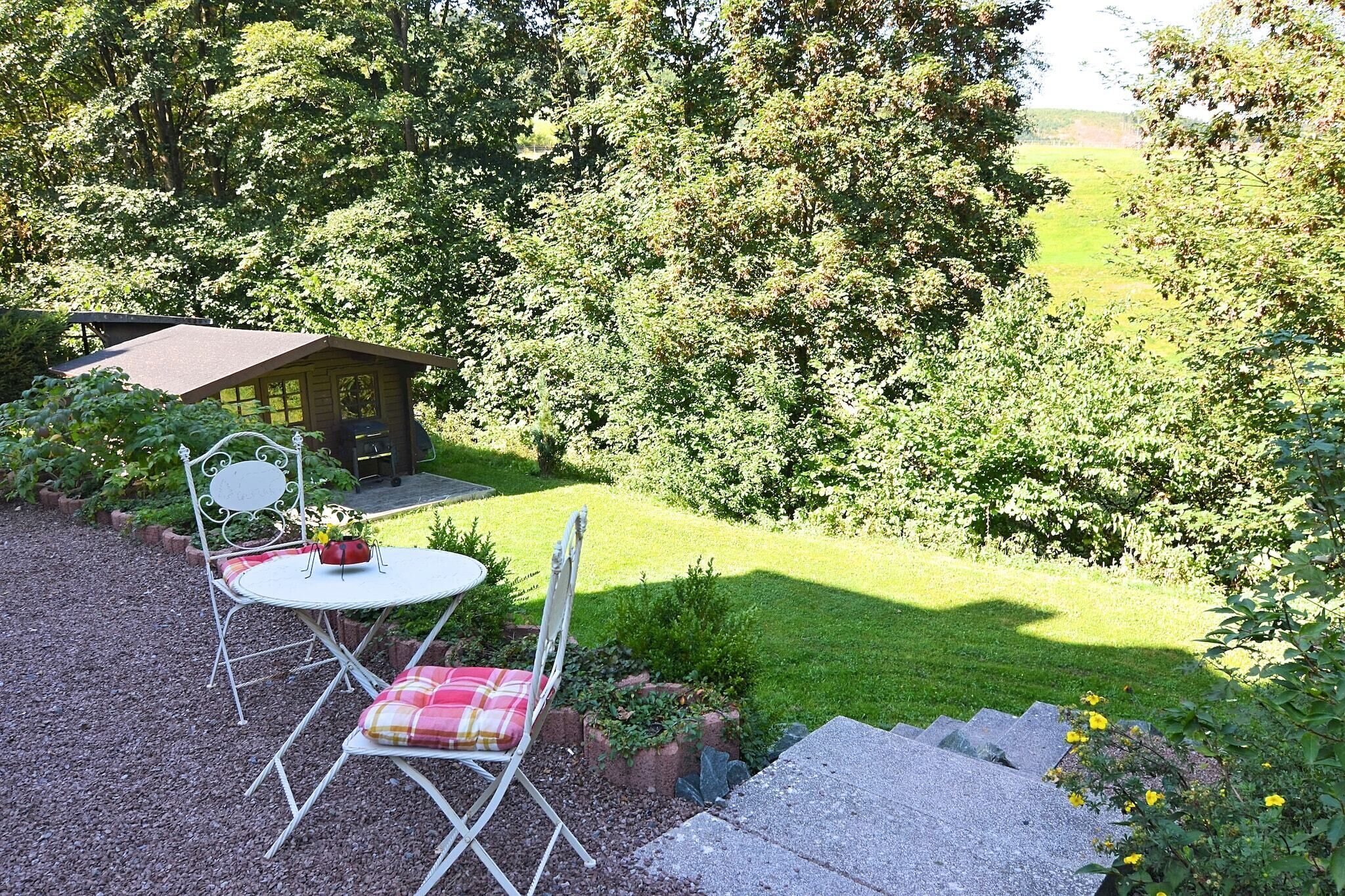 A patio with a table and chairs, a small shed, and a grassy area with trees in the background.