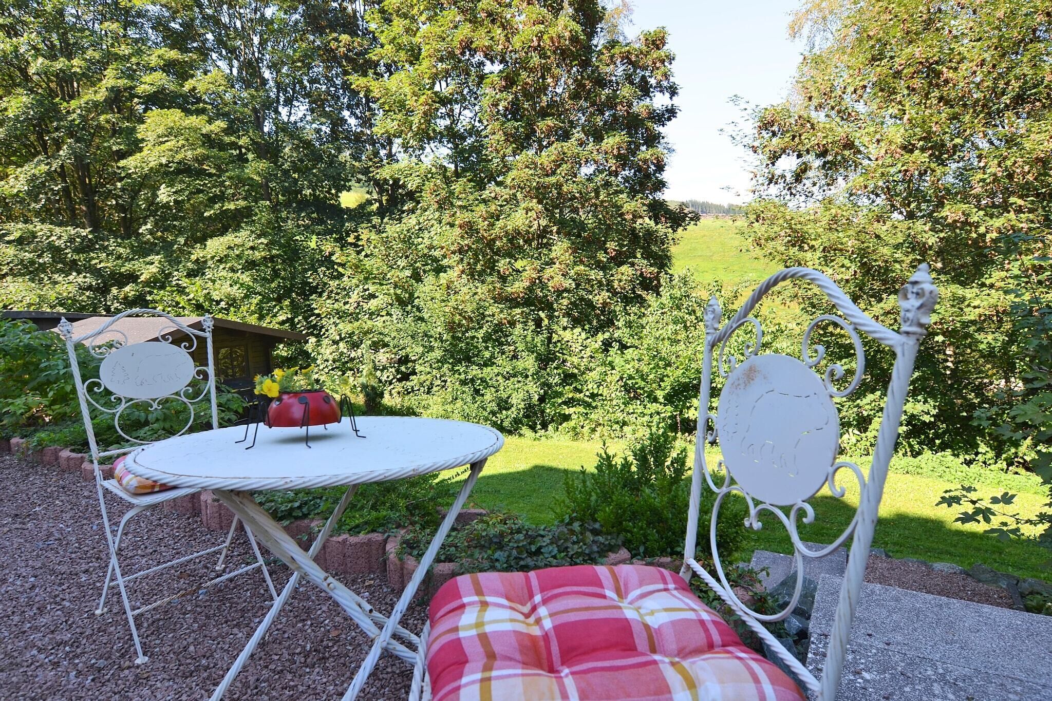 A garden setting with a metal table and chairs, surrounded by lush greenery and trees.