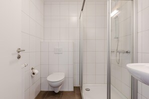 Een moderne badkamer met toilet, douche en wastafel.