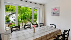 A dining area with a table set for four, a window with curtains, and a painting on the wall. - Ferienhaus Bergfreiheit (Winterberg)