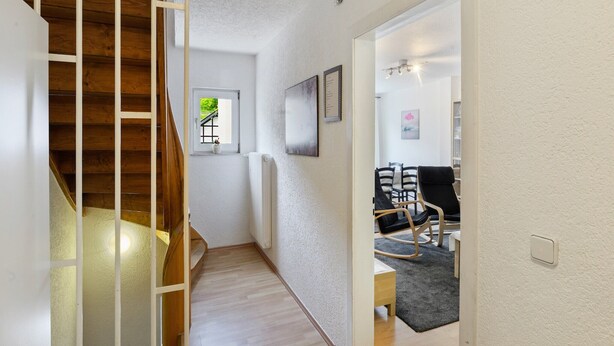 A hallway with a wooden staircase, a small window with a view, and a seating area with chairs and a table. - Ferienhaus Bergfreiheit (Winterberg)