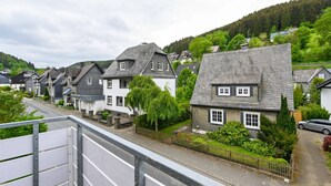 A row of traditional houses with stone roofs, a paved road, and a green hillside in the background. - Ferienhaus Bergfreiheit (Winterberg)