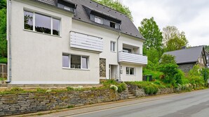 A two-story house with a stone wall, a balcony, and a road in front. - Ferienhaus Bergfreiheit (Winterberg)