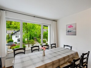 A dining room with a table set for four, large windows with curtains, a radiator, and a painting on the wall.