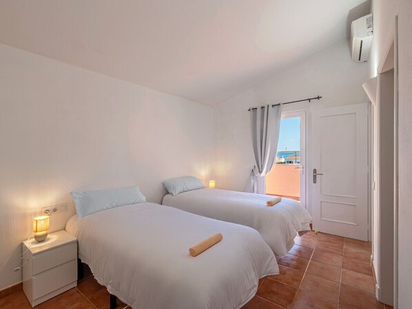 Une chambre avec deux lits, une table de chevet avec une lampe, une porte donnant sur un balcon extérieur et un climatiseur fixé au mur.