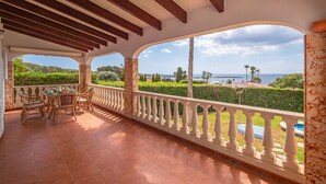 A covered outdoor patio with a dining area, white balustrades, and a scenic view of the sea and greenery. - Villa Sur A bit closer to heaven (Binisafua)