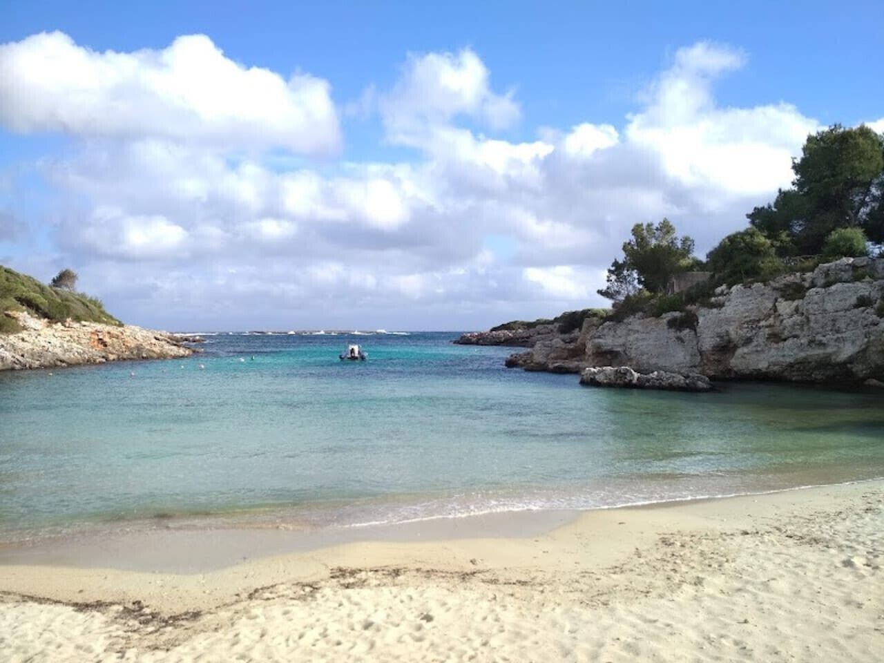A beach with clear water, a rocky shoreline, and a boat in the distance.