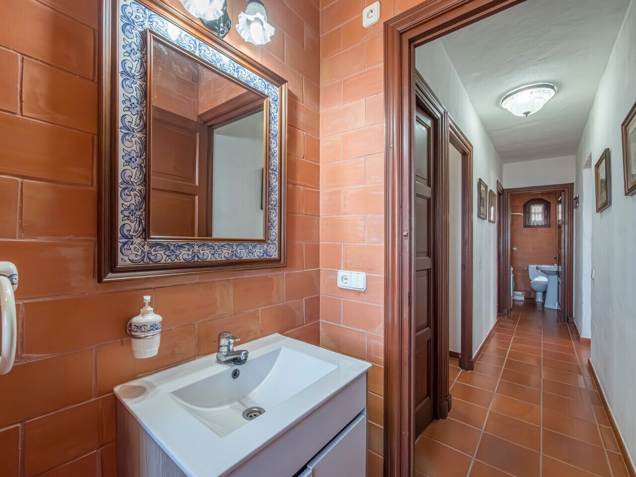 A bathroom with a white sink, a mirror with a decorative frame, and a soap dispenser on the wall.