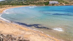 A coastal beach with clear waters, a sandy shore, and a building in the background. - Apt. Alcor, simply Mediterranean (Platges de Fornells)
