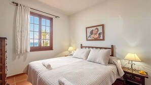 A neatly made bed with a white duvet, a bedside lamp, and a framed picture on the wall. - Apt. Alcor, simply Mediterranean (Platges de Fornells)