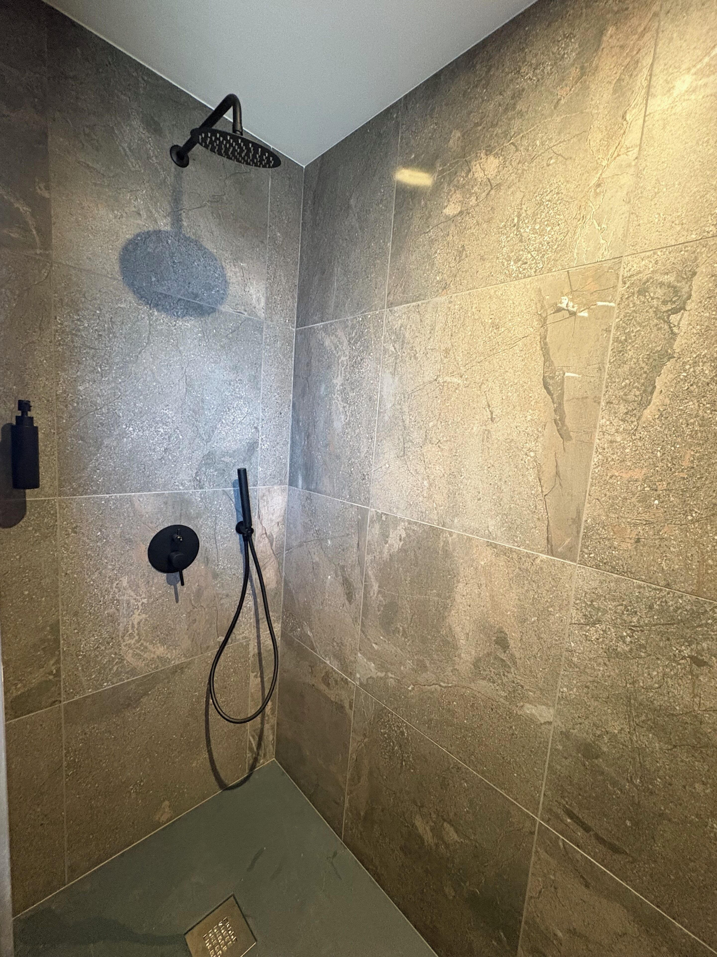 A shower with a handheld showerhead, a wall-mounted control, and a handheld hose.