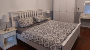 Un dormitorio ordenado con cama, mesitas de noche, un armario y una araña.