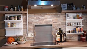 Una cocina con horno empotrado, estufa y varios electrodomésticos. Hay estantes con frascos y botellas, y una cesta en la encimera.