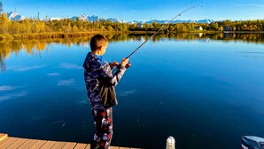 A person fishing by a calm lake with a clear view of mountains and houses in the background.