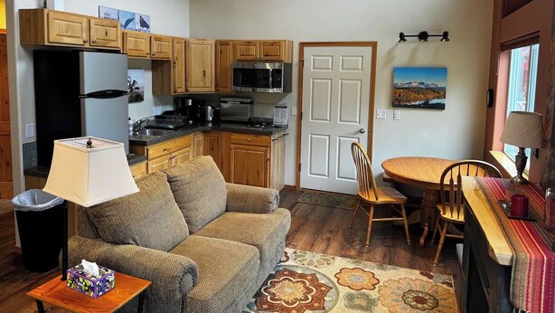 A compact living space with a kitchenette, a dining area with a wooden table and chairs, a sofa, and a lamp.