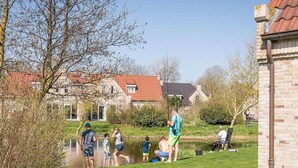 A group of people fishing by a pond, with houses and a brick building in the background. - Villa in Texel near De Krim Holiday Park (De Cocksdorp Texel)