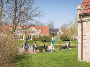 A group of people fishing by a pond, with houses and a brick building in the background. - Villa in Texel near De Krim Holiday Park (De Cocksdorp Texel)