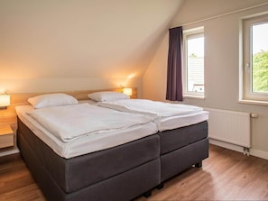 Et soveværelse med to senge, et vindue med gardiner, en radiator og et natbord med en lampe.