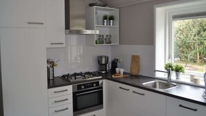 Une cuisine moderne avec des meubles blancs, une cuisinière à gaz, un four encastré, une machine à café et une fenêtre donnant sur un paysage verdoyant.