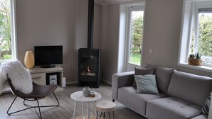 Un salon comprenant un canapé, un fauteuil, une petite table, un téléviseur et un poêle à bois.