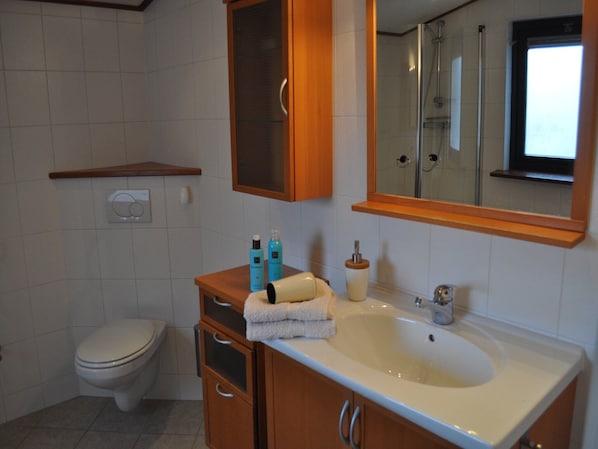 Een badkamer met toilet, wastafel en spiegel. Toiletartikelen staan op het aanrecht.