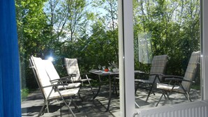 Een terras met tuinmeubilair, een tafel en uitzicht op bomen door een glazen deur.