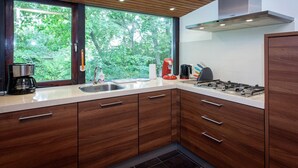 Een moderne keuken met houten kastjes, een roestvrijstalen spoelbak, een Bosch afzuigkap en een raam met uitzicht op groen.