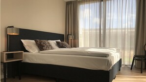 A modern hotel room with a large bed, two bedside tables, a lamp, and a view of the outdoors through sheer curtains. - Villa near Texel Beach with Sauna (De Koog)